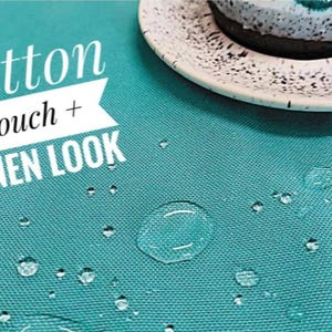 May include: A solid teal fabric with a woven texture featuring water droplets on the surface. The text "cotton touch + LINEN LOOK" is printed in white on the left side. A speckled white and black plate with a dark dessert sits in the corner.
