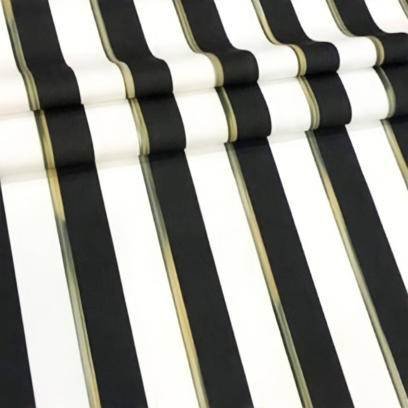 May include: Close-up of a fabric with a bold black and white striped pattern. The stripes are vertical and alternate in color. A thin gold-colored line separates the black and white stripes. The fabric is folded over itself.