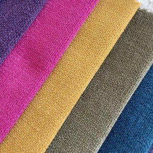 May include: A close-up of six fabric swatches in different colors and textures. The swatches are arranged in a diagonal pattern, with the darkest color at the bottom and the lightest color at the top. The colors are purple, pink, yellow, green, blue, and gray.