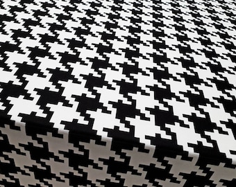 May include: A close-up of a fabric featuring a black and white houndstooth pattern. The design is a repeating arrangement of interlocking shapes, producing a classic and striking visual texture. The fabric appears smooth.