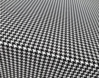 May include: A close-up of a black and white houndstooth fabric. The fabric has a repeating pattern of small, abstract shapes in black against a white background. This classic design is often used in clothing and interior design.