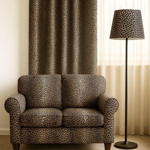 May include: A two-seater loveseat upholstered in a brown and black leopard print fabric, featuring rounded arms and dark wooden legs. Beside it stands a floor lamp with a matching leopard print lampshade and a thin, dark metal pole base.