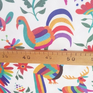 May include: White fabric with a colorful Mexican folk art design featuring birds, deer, and flowers. The fabric is measured with a ruler showing 60 inches.