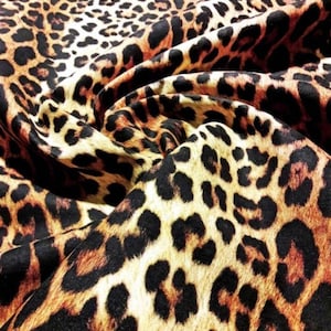 May include: Close-up of a brown, black, and cream leopard print fabric. The fabric is folded and has a soft, plush texture.