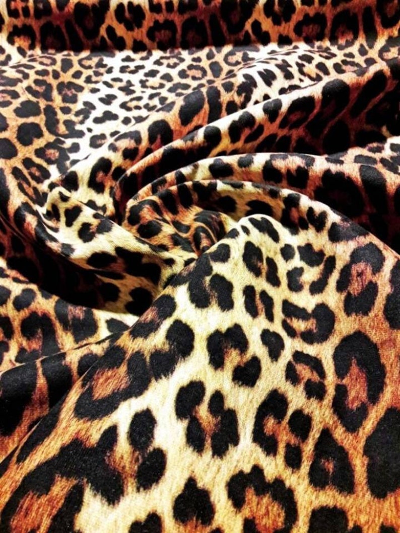 May include: Close-up of a brown, black, and cream leopard print fabric. The fabric is folded and has a soft, plush texture.