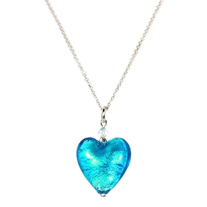 Puede incluir: Un collar de cadena de plata con un colgante de corazón de vidrio azul. El corazón tiene un acabado brillante e iridiscente.