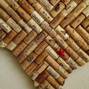 Może przedstawiać: Dzieło sztuki w kształcie Teksasu wykonane z kork&oacute;w do wina, ułożonych we wz&oacute;r jodełki. Korki prezentują r&oacute;żne nazwy i logo winnic. Mała czerwona gwiazda umieszczona jest na środku.