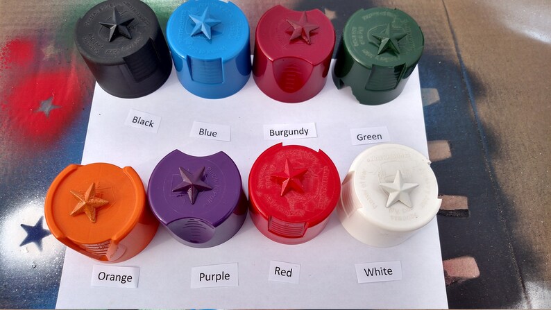 Może przedstawiać: Kolekcja kolorowych kork&oacute;w do butelek w kolorach czarnym, niebieskim, bordowym, zielonym, pomarańczowym, fioletowym, czerwonym i białym. Każdy korek ma gwiazdę na g&oacute;rze i jest oznaczony kolorem. Korki są ułożone na białej powierzchni.