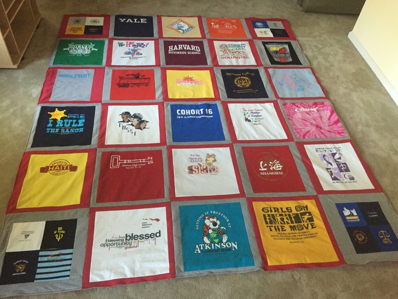 May include: A quilt made from a variety of t-shirts, featuring logos and text from different organizations and events. The quilt is made up of 25 squares, each with a different design. Some of the designs include the words "Yale", "Harvard", "Cohort 16", "I Rule the Ranch", "Haiti", "Blessed Opportunity", "Girls on the Move", and "Shanghai".