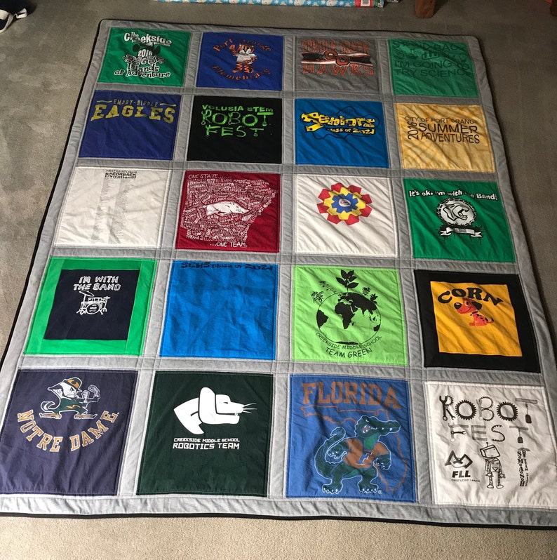 May include: A quilt made from a variety of t-shirts, featuring logos and text from different organizations and events. The quilt is made up of 16 squares, each with a different design. Some of the designs include a robot, a band, a school logo, and a state flag. The quilt is a great way to commemorate special events and memories.
