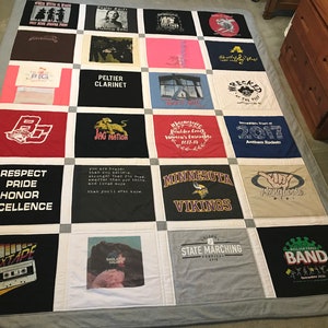 May include: A quilt made from a variety of t-shirts, featuring different designs and logos. The quilt is made up of 25 squares, each with a different t-shirt design. Some of the designs include a school mascot, a band logo, and a sports team logo. The quilt is a great way to commemorate special events or to show off your favorite teams and bands.