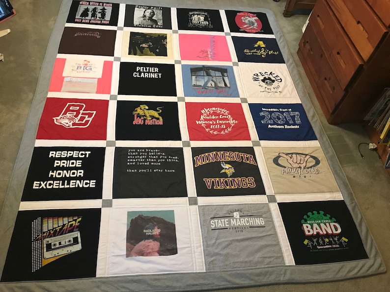 May include: A quilt made from a variety of t-shirts, featuring different designs and logos. The quilt is made up of 25 squares, each with a different t-shirt design. Some of the designs include a school mascot, a band logo, and a sports team logo. The quilt is a great way to commemorate special events or to show off your favorite teams and bands.