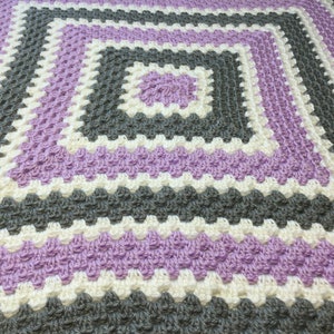 May include: A crocheted baby blanket with a square pattern in shades of purple, white, and gray.