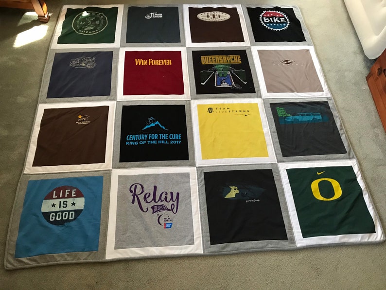 May include: A quilt made from a variety of t-shirts, featuring logos and text such as "Life is Good", "Win Forever", "Queensryche", "Century for the Cure", "Relay", "Team Livestrong", and "Bike".