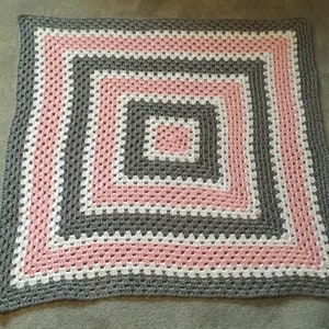 May include: A crocheted baby blanket with a square design in pink, white, and gray.
