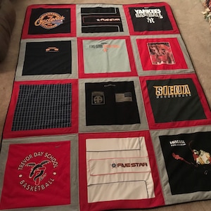 May include: A red, white, and gray quilt made from t-shirts. The quilt has a variety of logos and designs, including "Trevor Day School Basketball", "Five Star", "Yankees Baseball", "Silenza", and "Cleveland".
