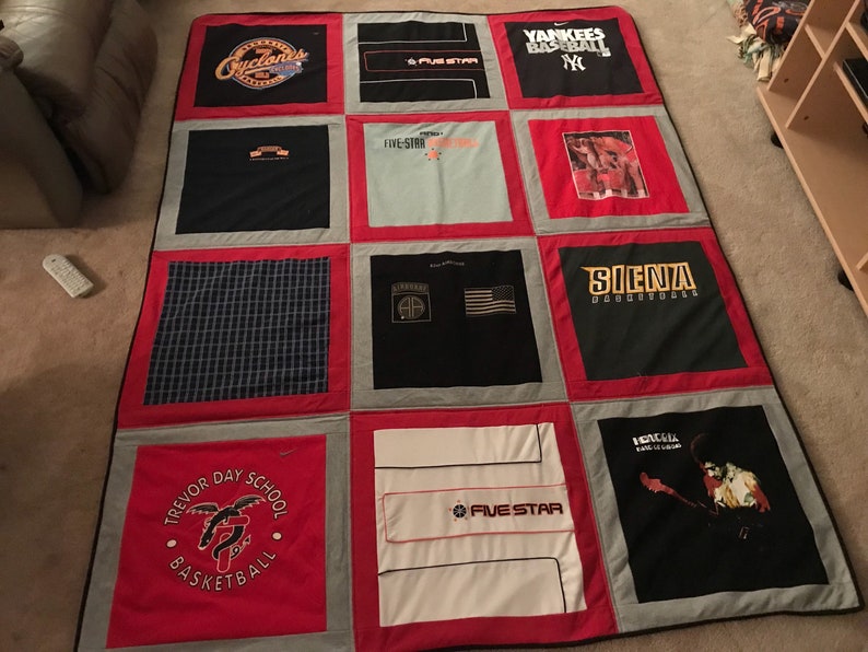 May include: A red, white, and gray quilt made from t-shirts. The quilt has a variety of logos and designs, including "Trevor Day School Basketball", "Five Star", "Yankees Baseball", "Silenza", and "Cleveland".