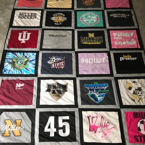 May include: A quilt made from a variety of t-shirts, featuring logos, text, and designs. The quilt is made up of 16 squares, each with a different design. Some of the designs include a soccer ball, a state cup, a fight like a champ logo, and a number 45.