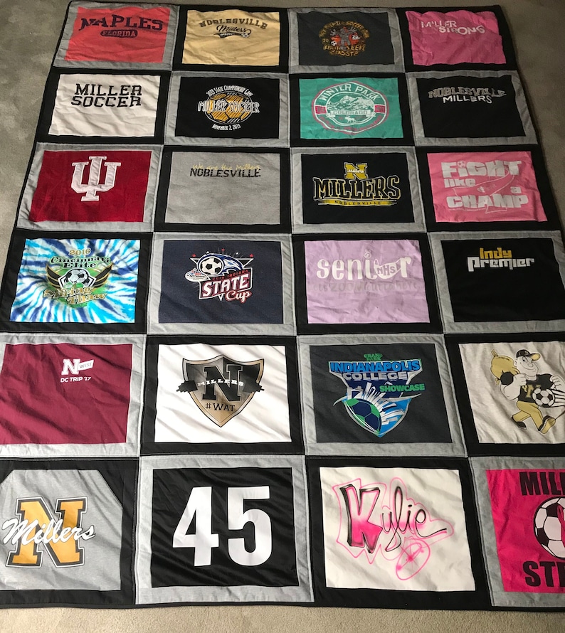 May include: A quilt made from a variety of t-shirts, featuring logos, text, and designs. The quilt is made up of 16 squares, each with a different design. Some of the designs include a soccer ball, a state cup, a fight like a champ logo, and a number 45.