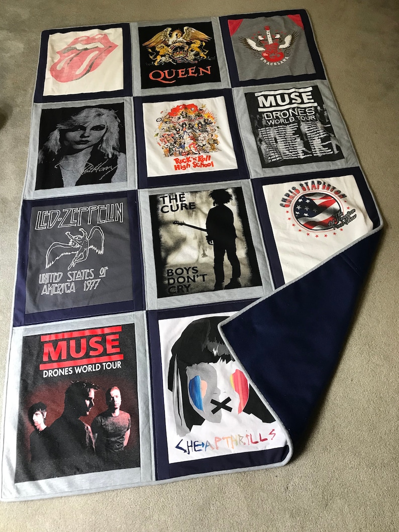 May include: A quilt made from various band t-shirts, including Queen, Muse, The Cure, Led Zeppelin, and Cheap Thrills. The quilt is made of a gray fabric with navy blue borders.