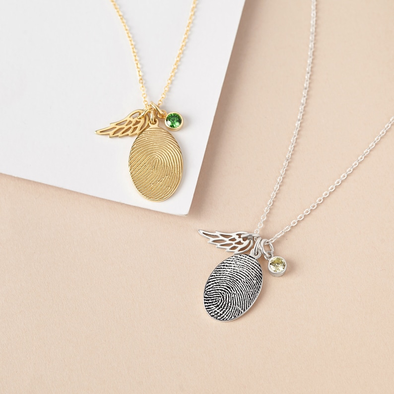 Two beautiful necklaces showcasing gold and silver fingerprint pendants, each with an angel wing and birthstone charm.