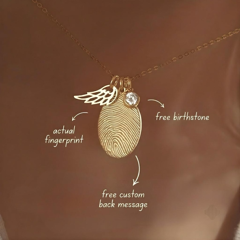 May include: A gold-toned necklace featuring an oval pendant engraved with an actual fingerprint, a small angel wing charm, and a clear round birthstone. Text on the image reads: actual fingerprint, free birthstone, and free custom back message.
