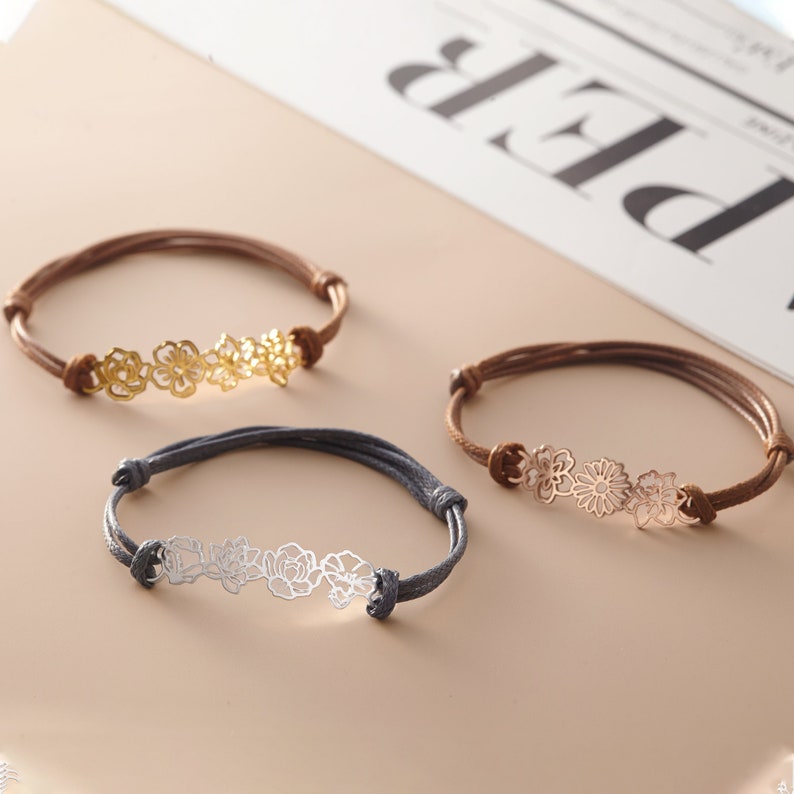 May include: Three adjustable bracelets with floral designs. One bracelet has a gold-colored floral design on a brown cord. Another has a silver-colored floral design on a gray cord. The third has a rose gold floral design on a brown cord.