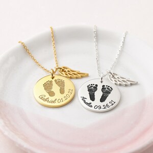 Puede incluir: Dos collares personalizados con colgantes redondos. Uno dorado con huellas de beb&eacute;, el nombre "Gabriel" y la fecha "01.20.22". El otro plateado con "Amelia" y "09.26.21". Cada uno tiene un dije de ala.