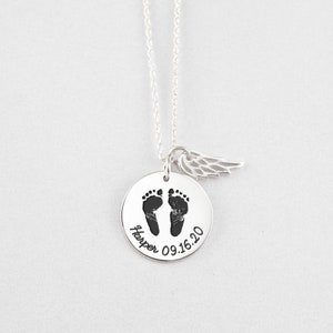 Puede incluir: Un collar de plata con un colgante redondo con huellas de beb&eacute; y el nombre "Harper" con la fecha "09.16.20". Un peque&ntilde;o dije de ala cuelga al lado. El collar est&aacute; sobre un fondo blanco.