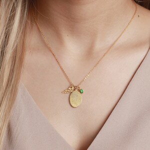 A model wearing a gold fingerprint necklace, complete with an angel wing and green birthstone charm, highlighting its elegant design.