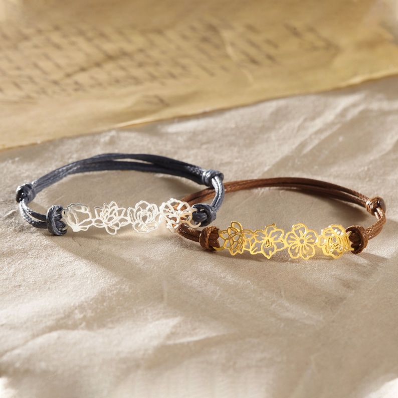 May include: Two bracelets with floral designs. One bracelet has a silver-colored floral design on a dark blue cord. The other bracelet has a gold-colored floral design on a brown cord. Both bracelets are adjustable.