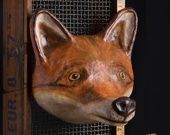 Könnte beinhalten: Eine handgefertigte Fuchskopfskulptur in Orange-, Braun- und Cremetönen. Der Kopf ist auf einem Holzrahmen mit Drahtgitter befestigt. Ein Vintage-Zollstock, in Zentimetern, befindet sich daneben. Ein kleiner Metalleimer mit getrockneten Blumen ist ebenfalls vorhanden.