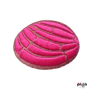 Puede incluir: Parche de plancha bordado de color rosa con forma de concha, un pan dulce mexicano tradicional.