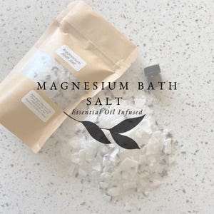 Peut inclure: Un sac en papier brun rempli de sels de bain blancs, étiqueté "Magnesium Bath Salt Essential Oil Infused". Une petite bouteille en verre brun avec un bouchon noir est à côté du sac.