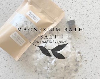 Può includere: Un sacchetto di carta marrone pieno di sali da bagno bianchi, etichettato "Magnesium Bath Salt Essential Oil Infused". Una piccola bottiglia di vetro marrone con un tappo nero è accanto al sacchetto.