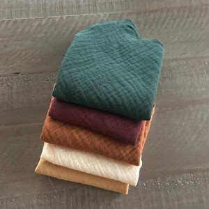 Peut inclure: Une pile de cinq tissus carr&eacute;s pli&eacute;s pr&eacute;sentant un tissage en mousseline textur&eacute; et froiss&eacute;. Les couleurs, de haut en bas, sont le vert for&ecirc;t fonc&eacute;, le bordeaux profond, l'orange br&ucirc;l&eacute;, le blanc cass&eacute; et le jaune moutarde dor&eacute;.