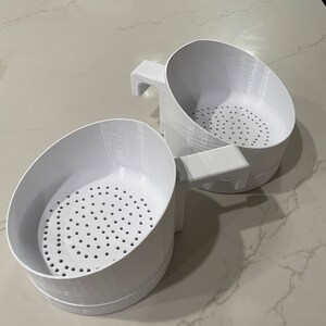 May include: Two white plastic kitchen strainers with handles. The strainers have a mesh bottom with small holes.