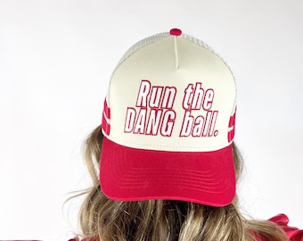 May include: A red and white trucker hat with the text "Run the DANG ball." The hat has a red brim and a white mesh back. The text is embroidered in red.