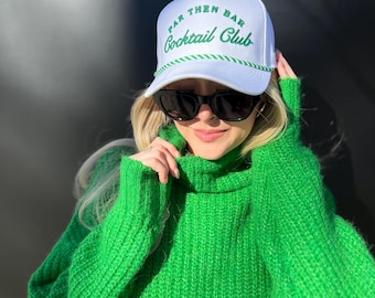 May include: A white baseball cap with a green embroidered logo that says "Par Then Bar Cocktail Club". The person wearing the cap is also wearing a bright green sweater.