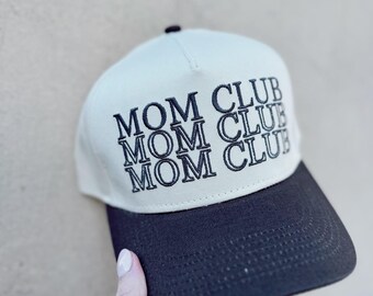 May include: A beige and black baseball cap with the text "MOM CLUB" embroidered on the front in black.