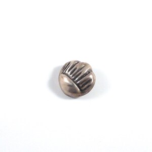 May include: A silver button with a raised, textured design resembling a flower or a crown.