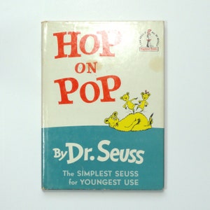 May include: A vintage children's book titled "Hop on Pop" by Dr. Seuss. The cover features a yellow bear with three red and yellow bears on its back. The book is part of the Beginner Books series.