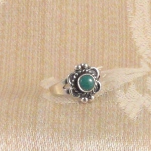May include: A silver ring with a green gemstone set in a floral design.