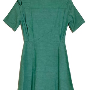 Puede incluir: Un vestido verde de manga corta con cuello y un parche en el hombro izquierdo que dice "Girl Scouts USA".