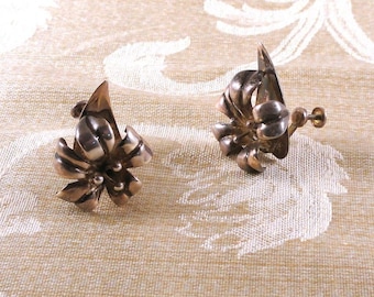 May include: A pair of silver flower-shaped clip-on earrings. The earrings are made of a textured metal and have a delicate design.