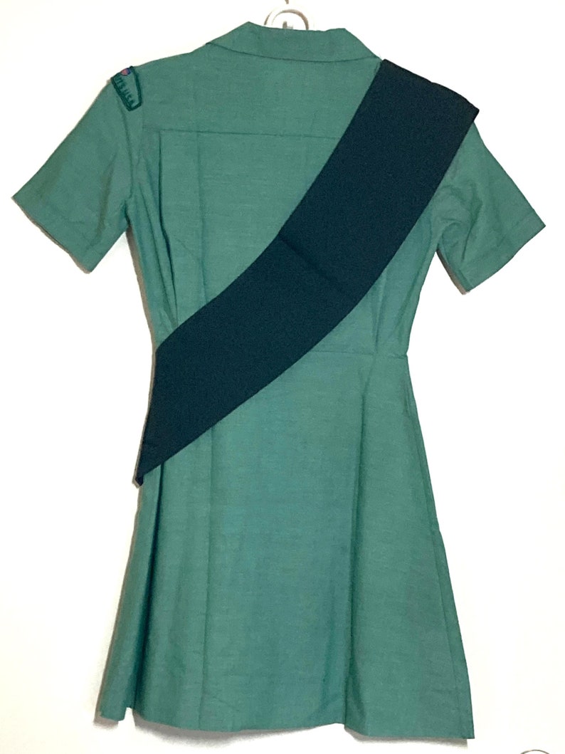 Puede incluir: Un vestido verde con mangas cortas y una faja negra. El vestido tiene cuello y cierre de botones.