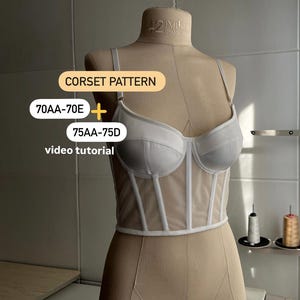 Op de afbeelding: Wit mesh corsetpatroon met een witte stofbuste. Het patroon is voor de maten 70AA-70E en 75AA-75D. De tekst "CORSET PATTERN" is in geel op een witte achtergrond geschreven. De tekst "video tutorial" is in zwart op een witte achtergrond geschreven.