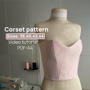 Puede incluir: Un corsé sin tirantes de color rosa pálido sobre un maniquí con el texto: Corset pattern, Sizes: 38, 40, 42, 44, Video tutorial, PDF-A4. Una gargantilla de encaje blanco rodea el cuello del maniquí y una máquina de coser Juki es visible.