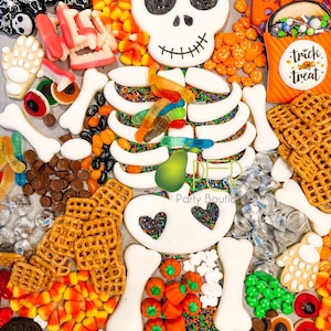May include: A Halloween-themed charcuterie board featuring a large central skeleton cookie surrounded by candy corn, gummy worms, chocolate drops, pretzels, silver-wrapped candies, pumpkin-shaped sweets, and cookies shaped like skulls and hands.