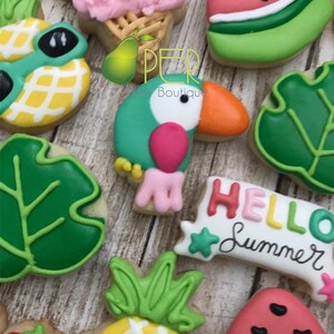 May include: Assortment of summer-themed cookies, including a toucan, watermelon slices, pineapple with sunglasses, and ice cream cone. The cookies are decorated with bright colors and the phrase "HELLO Summer".